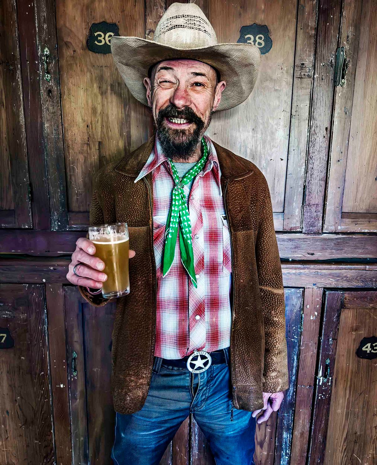 Portriat of a man that looks intoxicated in a locker room. His fly is undone and he holds a glass of beer.