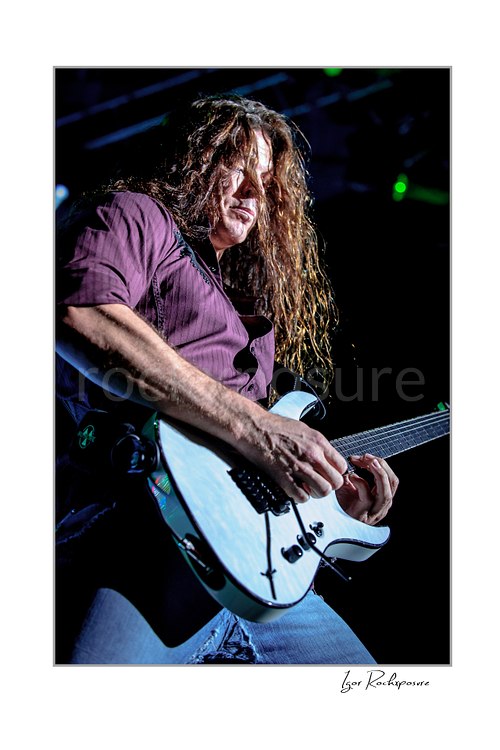 Vertical color image of Kiko Loureiro of Megadeth playing guitar in a tight low-angle stage close-up with long hair falling across his face