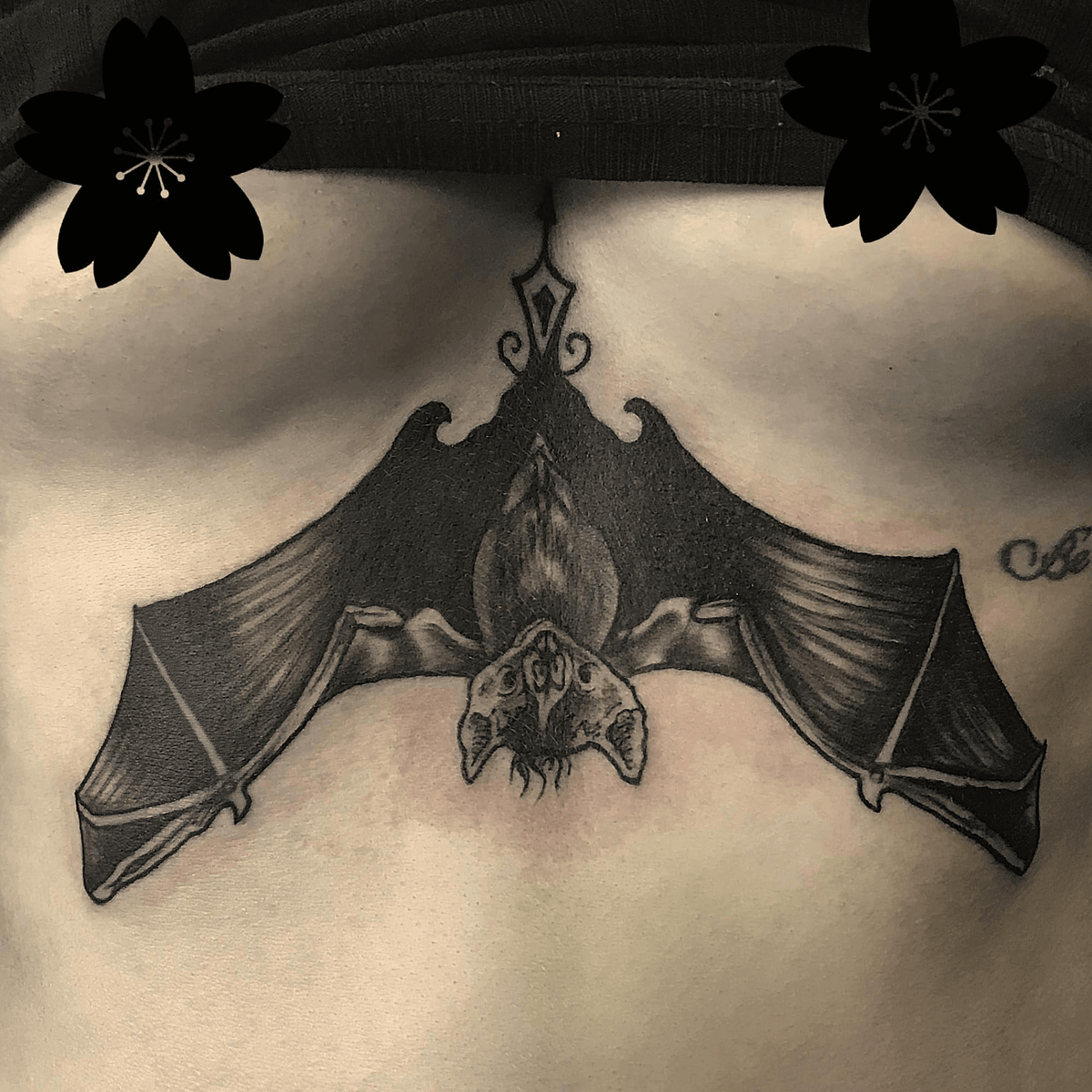 Neotraditional bat tattoo under the chest area with bold black linework and ornamental shading, symmetrical design created in Stoke-on-Trent by Alika Tattoo Art.