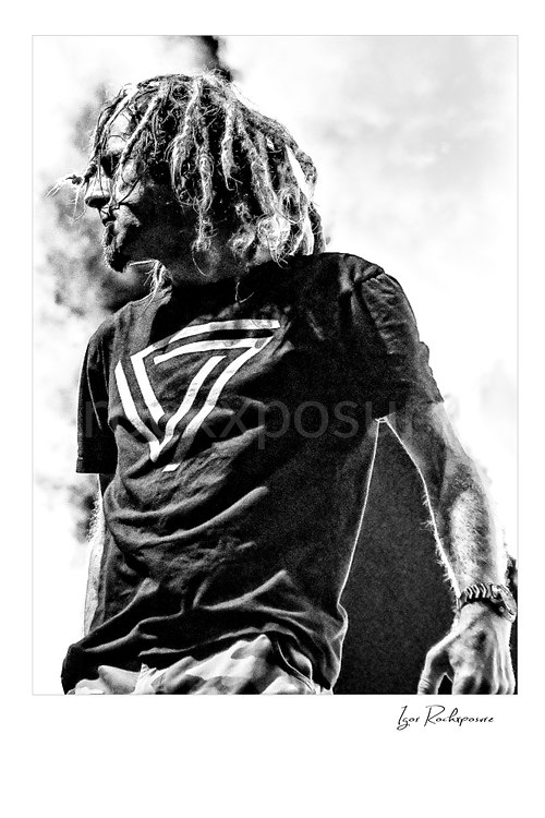 Vertical black and white image of Randy Blythe of Lamb of God standing on stage with dreadlocks and drifting smoke
