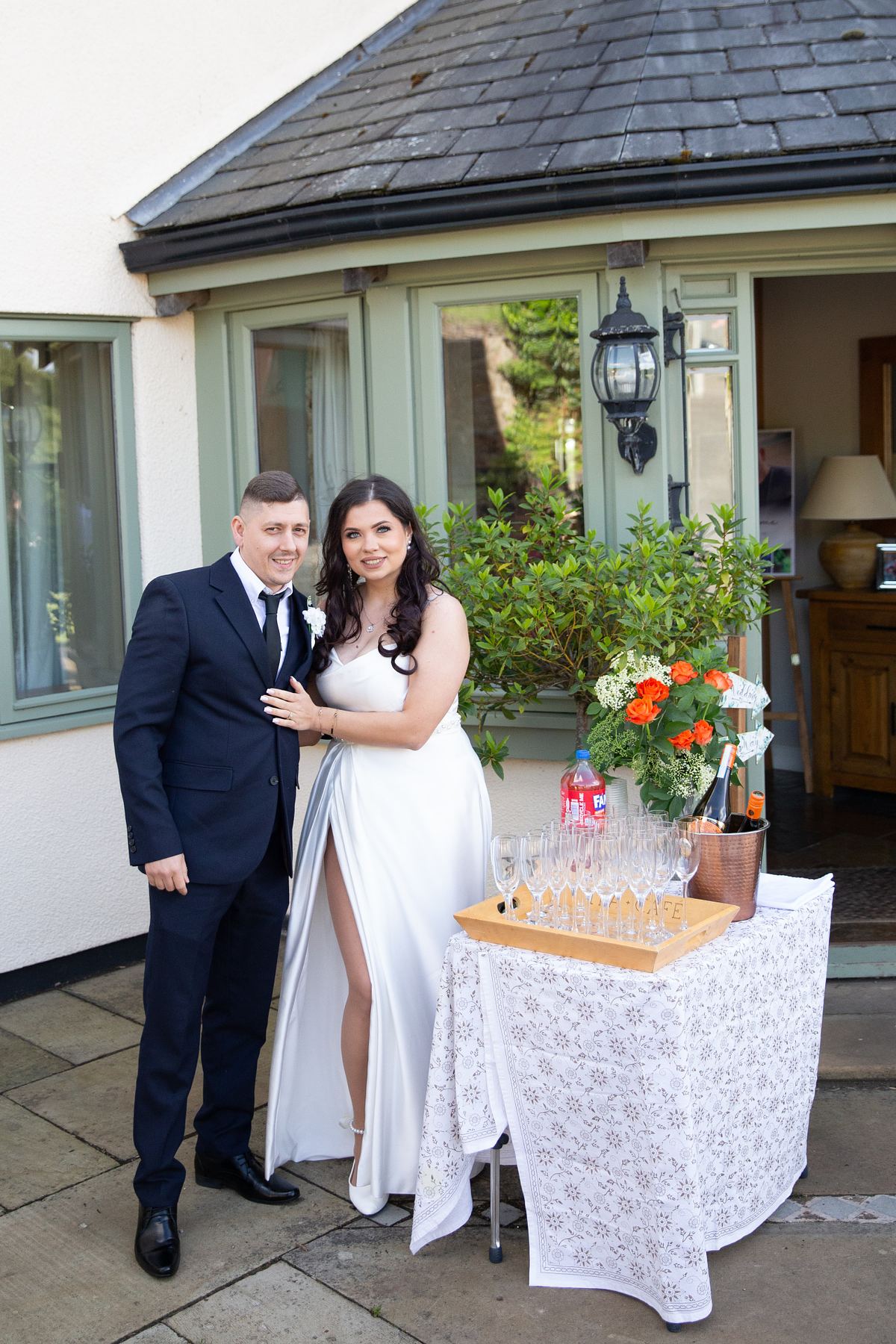 Bride and groom standing beside a drinks table outside a house in South Wales