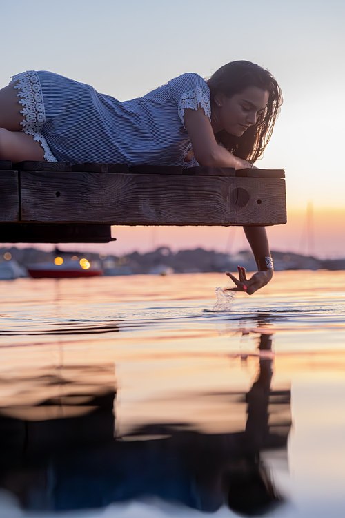 Femme allongée sur un ponton au-dessus de la mer avec son reflet dans l’eau