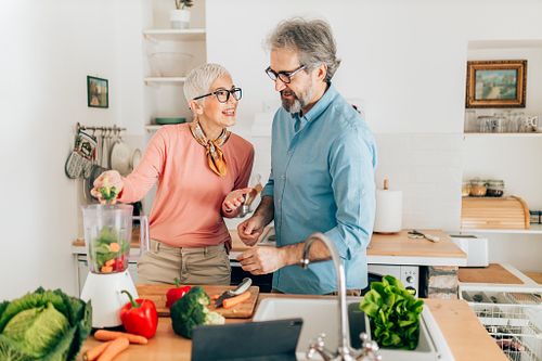 Senior couple preparing healthy smoothie in kitchen and using tablet to read recipe