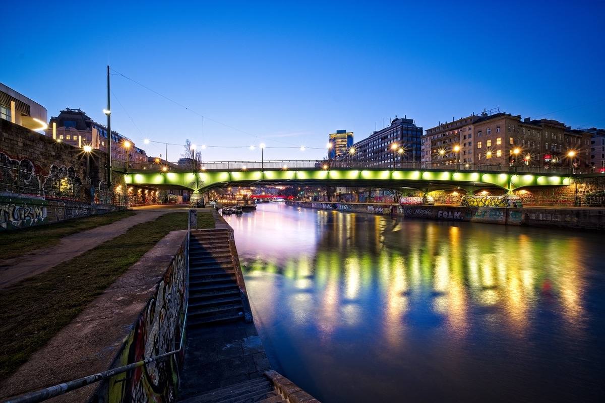 Fine-Art-Print des Wiener Donaukanals zur blauen Stunde mit beleuchteter Brücke, Street Art und Lichtreflexionen