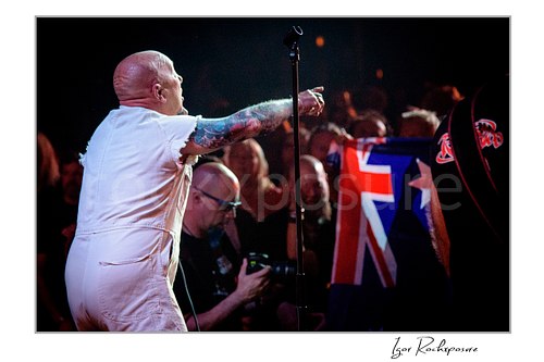 Horizontal color image of Angry Anderson of Rose Tattoo performing from the stage edge beside a microphone stand and pointing toward the crowd