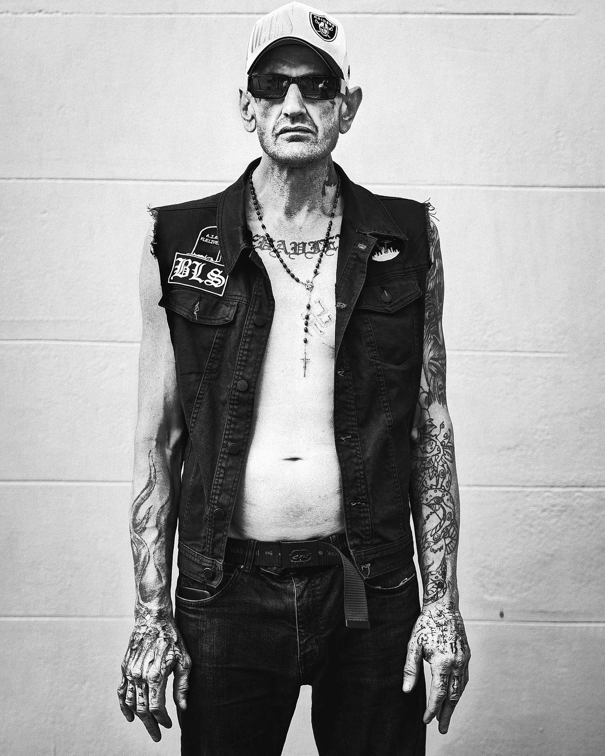 Portrait of a heavily tattooed man in a jacket with cut off sleeves.