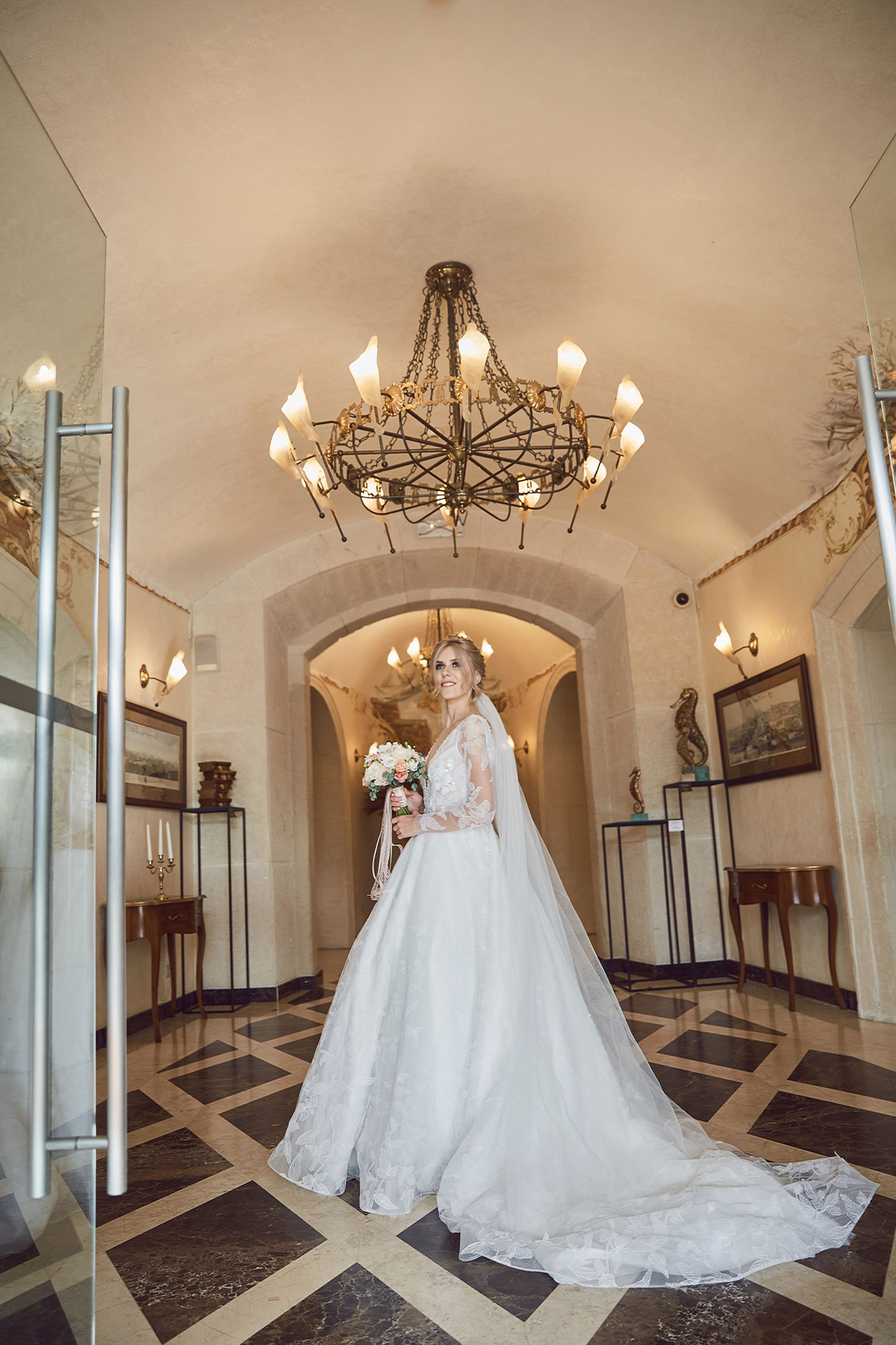 Full-length bridal portrait beneath an elegant chandelier at Citadel Inn