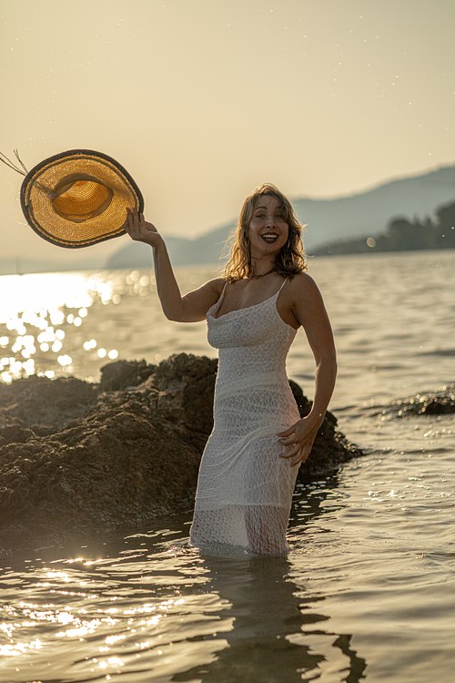 Femme jouant avec son chapeau dans la mer au coucher du soleil sur la côte varoise