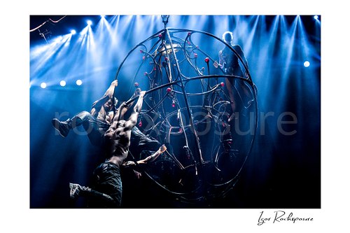 Horizontal color image of Pink with aerial acrobats on a suspended stage structure under bright blue concert beams