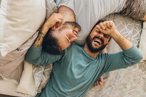 Happy gay couple lying down on the bed at home, hugging and flir