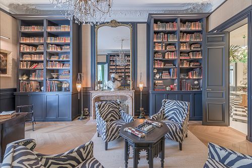 Bibliothèque et salon d’un appartement haussmannien de 400 m² rue du Faubourg Saint-Honoré avec fauteuils zèbre, cheminée et grandes bibliothèques bleues. Photographie d’architecture intérieure par Nicolas Karadimos.