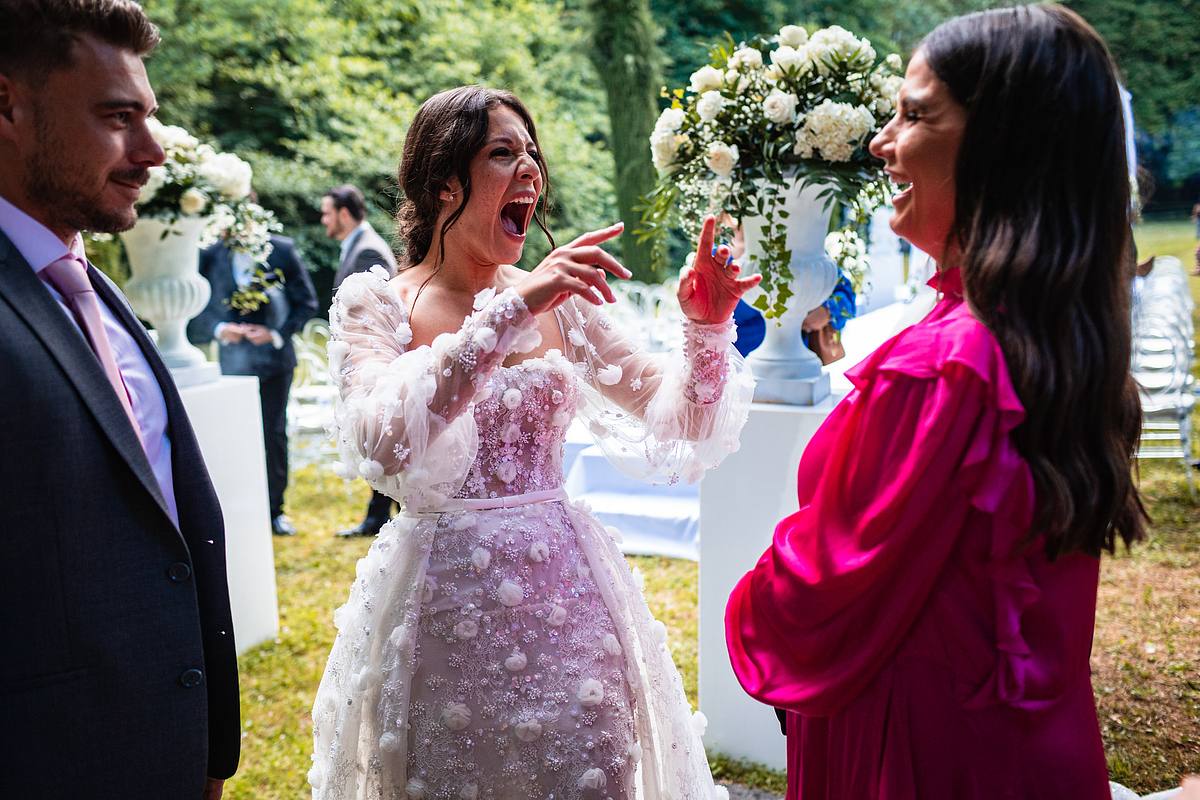 La mari&eacute;e &eacute;clate de rire en pointant du doigt, en partageant un moment joyeux avec une invit&eacute;e v&ecirc;tue de rose, une sc&egrave;ne de complicit&eacute; chaleureuse captur&eacute;e par Sebastien CLAVEL Photographe mariage Lyon
