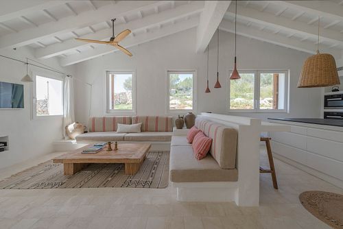 Salon lumineux avec banquettes intégrées, table basse en bois et ventilateur de plafond dans la finca Son Fonoll à Minorque. Photographie par Nicolas Karadimos.