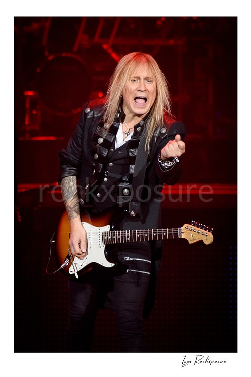 Vertical color image of Chris Caffery of Trans Siberian Orchestra performing live with an electric guitar against a red stage background