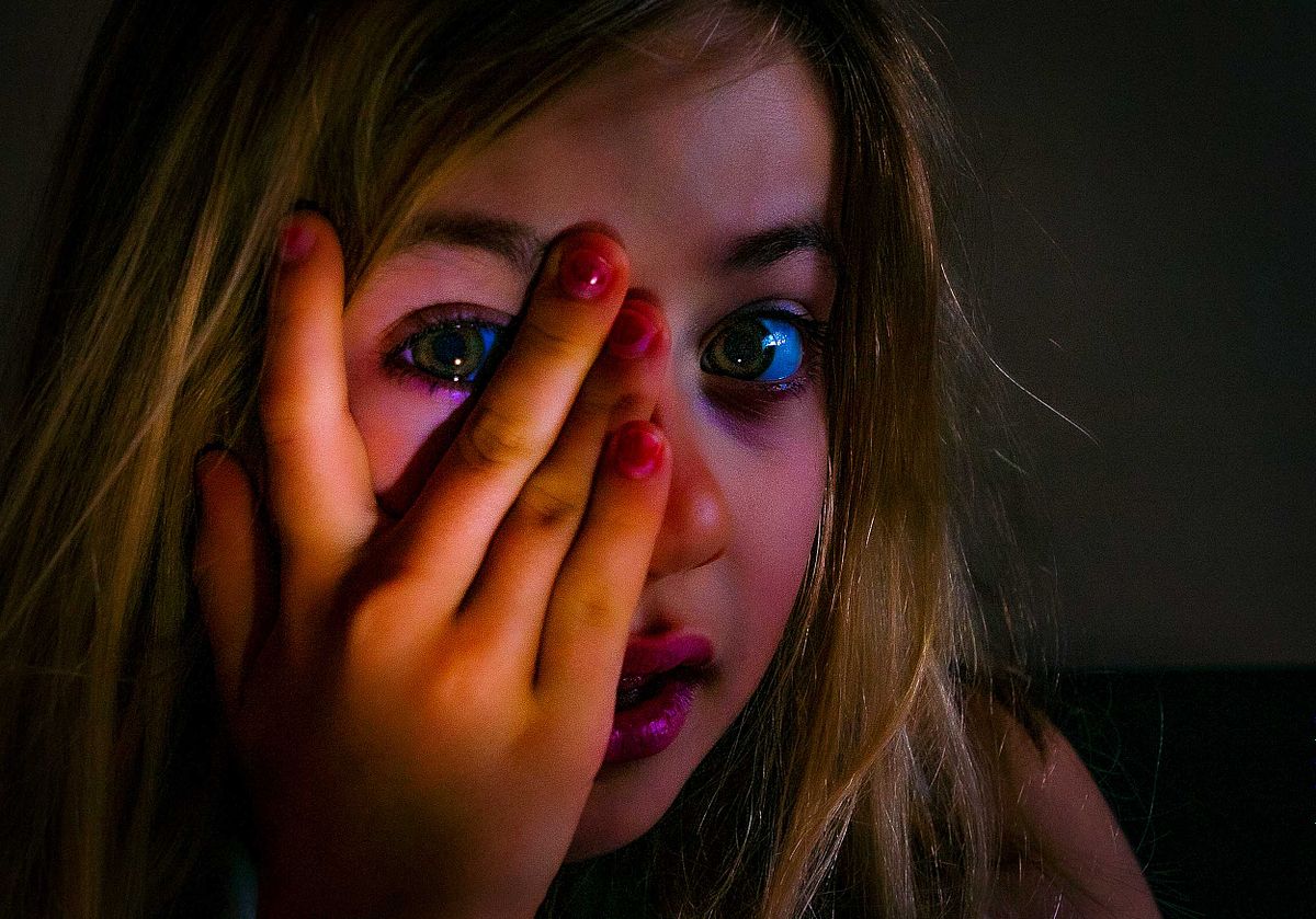 Portriat of a young girls lit with a torch. She looks through her fingers.