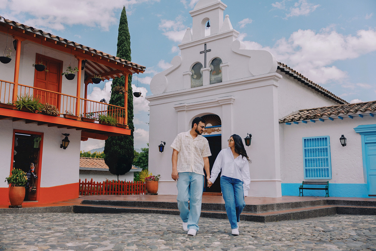 Couple walking past the white chapel at Pueblito Paisa during an engagement session