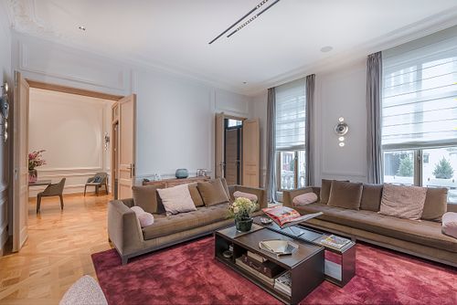 Salon haussmannien sur les Champs-Élysées avec canapés taupe, tapis rouge et grandes fenêtres. Photographie d’architecture intérieure par Nicolas Karadimos.