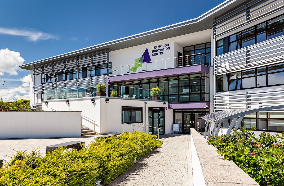 Tremough Innovation Centre stands with its modern architecture and glass facade amidst beautifully landscaped surroundings under a clear blue sky.