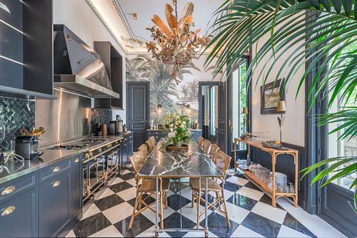 Cuisine et salle à manger d’un appartement haussmannien de 400 m² rue du Faubourg Saint-Honoré avec papier peint à motifs de palmiers, sol en damier et lustre en cristal. Photographie d’architecture intérieure par Nicolas Karadimos.