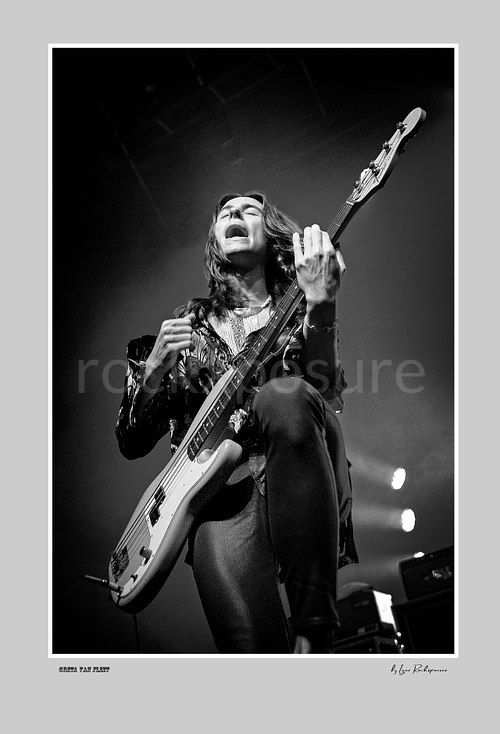 Vertical black and white image of Greta Van Fleet bassist Sam Kiszka performing live with his bass guitar