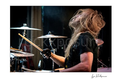 Horizontal color image of Robert Sweet of Stryper playing drums with flying hair during a live performance