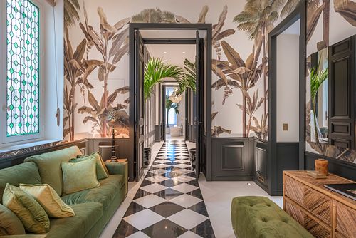 Entrée et couloir d’un appartement haussmannien de 400 m² rue du Faubourg Saint-Honoré avec papier peint à motifs de palmiers et sol en damier noir et blanc. Photographie d’architecture intérieure par Nicolas Karadimos.