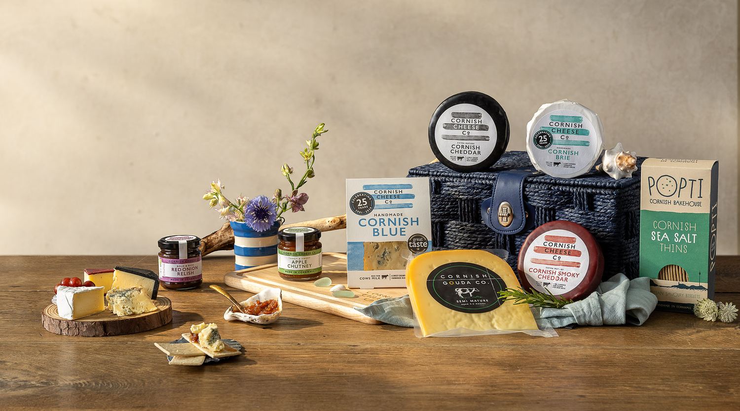 A studio image of a blue cornish hamper featuring different cheese and chutneys