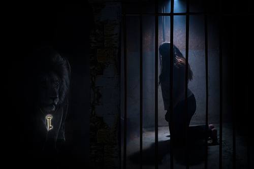 A woman behind bars looking toward a massive lion in the dark.