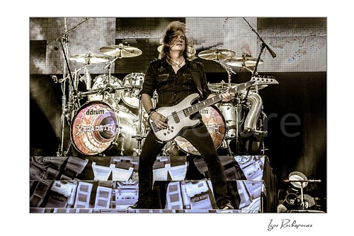 Horizontal color image of David Ellefson of Megadeth playing bass on stage in front of the drum kit