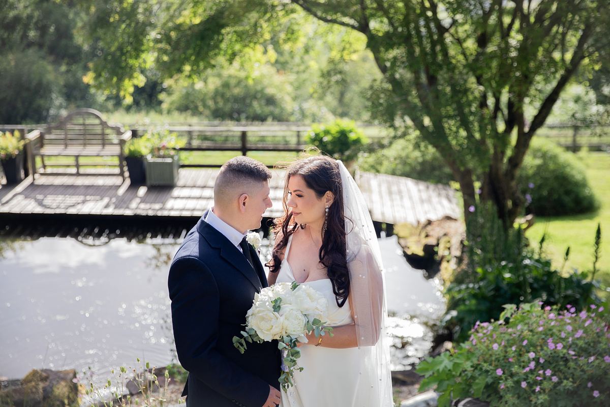 Bride and groom beside a garden pond surrounded by trees and flowers in South Wales