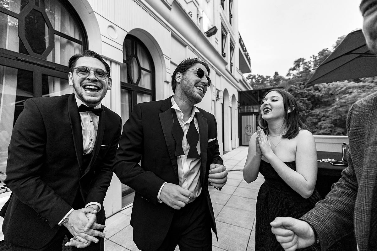 Un groupe d'invit&eacute;s chics partage un moment de joie communicative, riant aux &eacute;clats sous une lumi&egrave;re douce, une sc&egrave;ne captur&eacute;e avec brio par Sebastien CLAVEL Photographe mariage Lyon