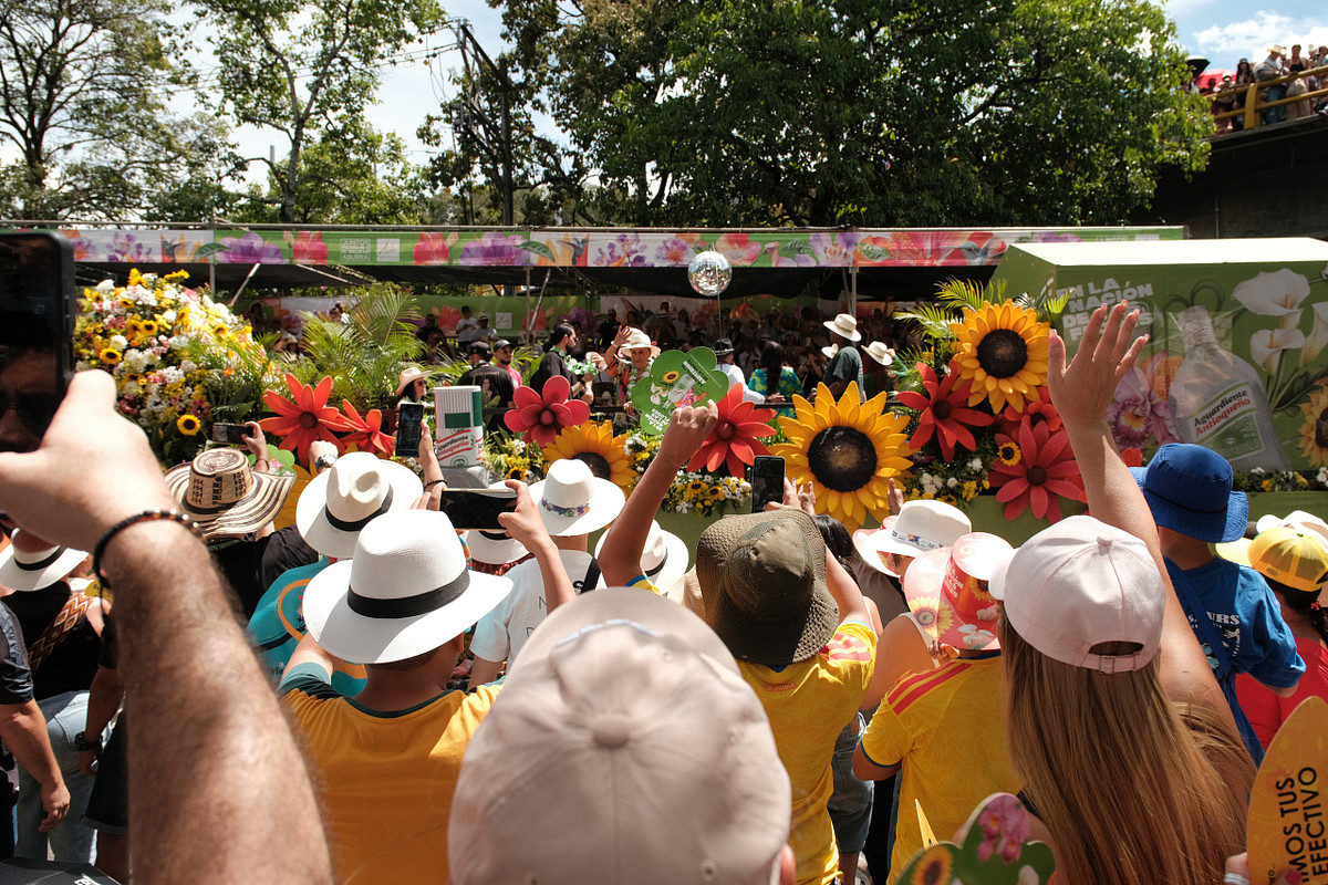 Crowd in paisa sombreros cheering beside a sunflower covered float at the Feria de las Flores