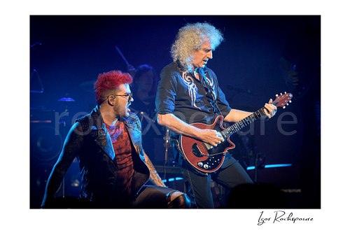 Horizontal color image of Adam Lambert and Brian May of Queen performing onstage together under cool blue concert lighting