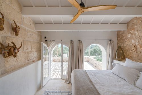 Chambre avec mur en pierre apparente et vue sur la terrasse dans la finca Son Fonoll à Minorque. Photographie par Nicolas Karadimos.