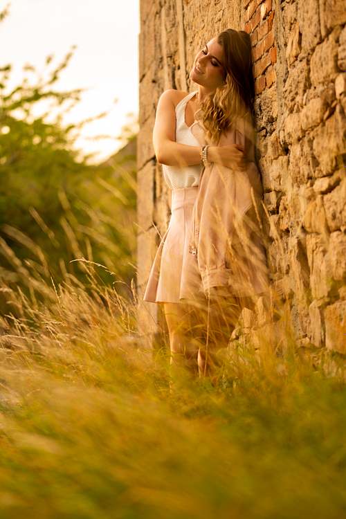 Porträt einer Frau im Sommerkleid an einer Steinmauer, hohes Gras im Vordergrund