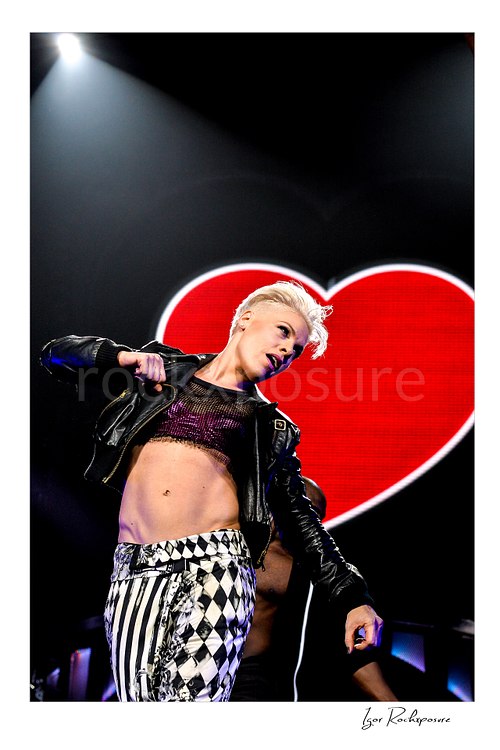 Vertical color image of Pink performing onstage before a glowing red heart backdrop under dramatic spotlight
