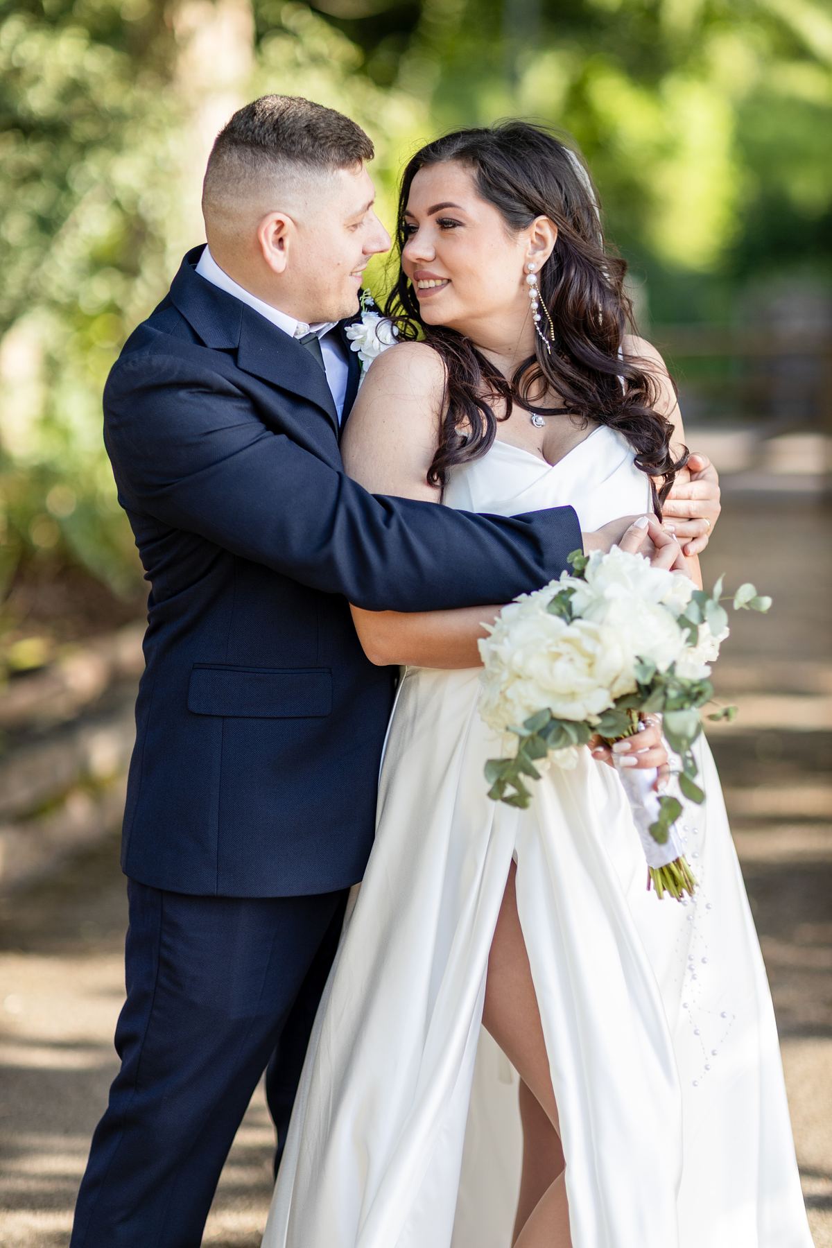 Bride and groom embracing outdoors among green trees in South Wales
