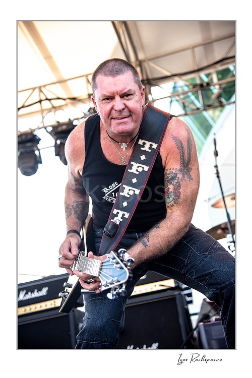 Vertical color image of an unidentified guitarist of Rose Tattoo playing guitar onstage in a tight outdoor live performance shot