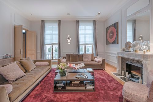 Salon haussmannien sur les Champs-Élysées avec canapé taupe, tapis rouge et cheminée. Photographie d’architecture intérieure par Nicolas Karadimos.