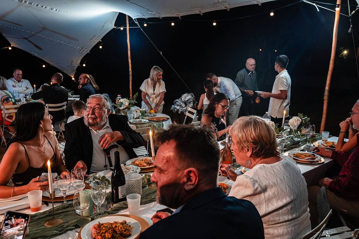 Invit&eacute;s de mariage profitant d'un d&icirc;ner sous une tente &eacute;clair&eacute;e, ambiance chaleureuse immortalis&eacute;e par S&eacute;bastien Clavel, photographe de mariage