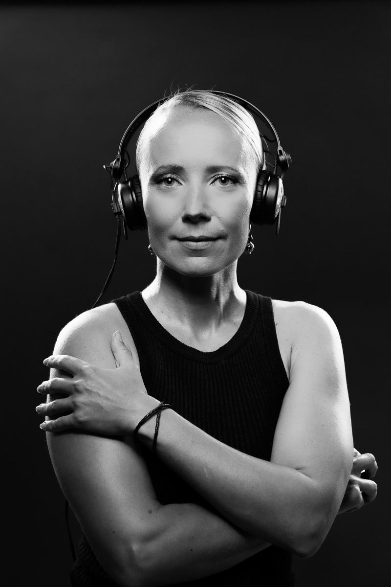 A black and white studio portrait of a female DJ wearing headphones