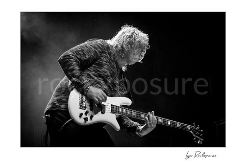 Horizontal black and white image of Billy Sherwood of Yes playing bass onstage in side profile through drifting stage smoke