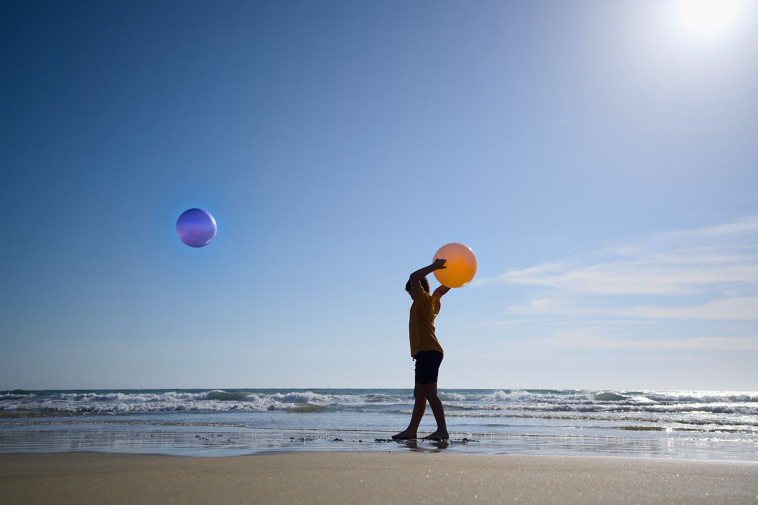 Child lifting a beach ball into the bright sky during a coastal portrait session.