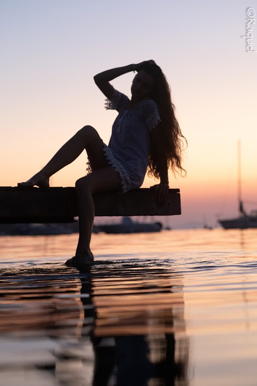 Jeune femme assise sur un ponton avec son reflet dans l'eau au coucher du soleil à Hyères.