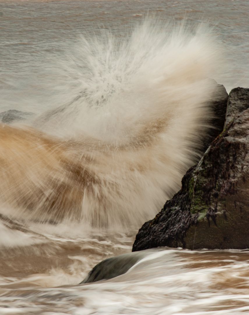 Breaking wave crashing against rocks on the Norfolk coast, captured as an intimate seascape detail.