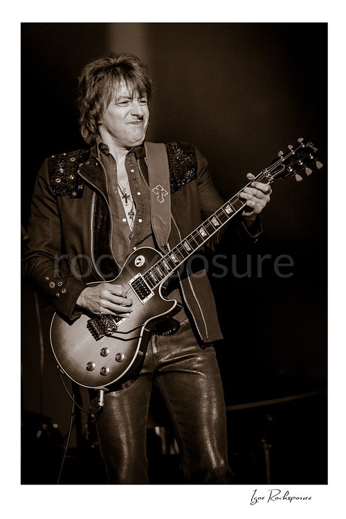 Vertical black and white image of Richie Sambora of Bon Jovi playing guitar on stage in a close live performance portrait