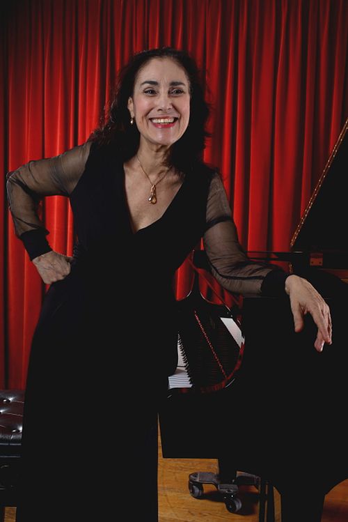 Myriam Birger at the piano after a concert, smiling in front of a stage curtain