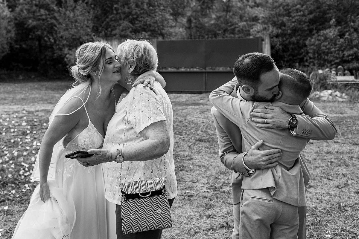 &Eacute;mouvante embrassade entre la mari&eacute;e et une invit&eacute;e, avec en arri&egrave;re-plan un mari&eacute; &eacute;changeant une accolade chaleureuse, immortalis&eacute;e par S&eacute;bastien Clavel, photographe de mariage