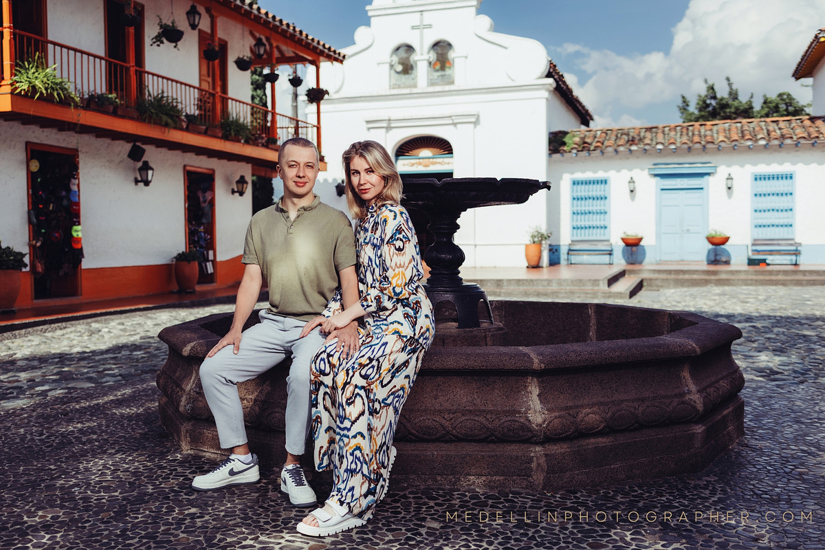 Couple seated on a stone fountain in a whitewashed colonial plaza in Medellin