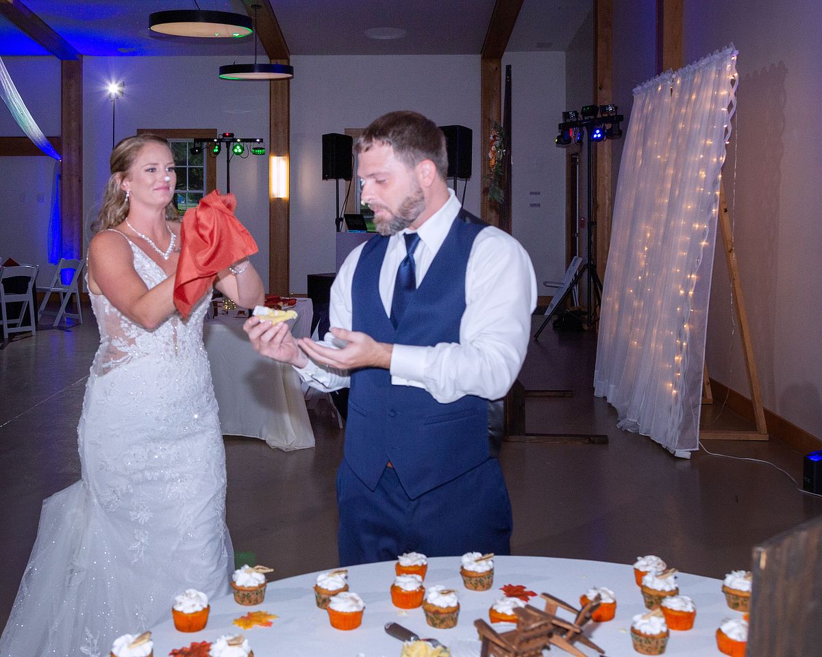 bride with cake on her nose pretending to clean up her groom after cake cutting
